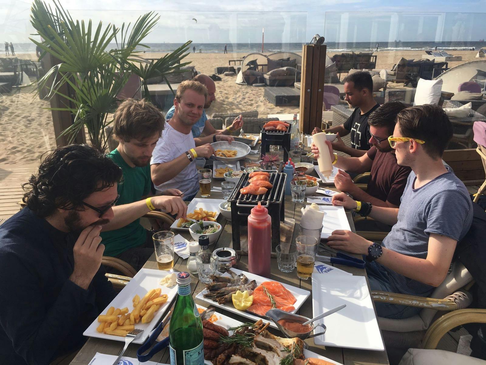 Een groep mannen zit aan het strand aan een tafel te barbecuen