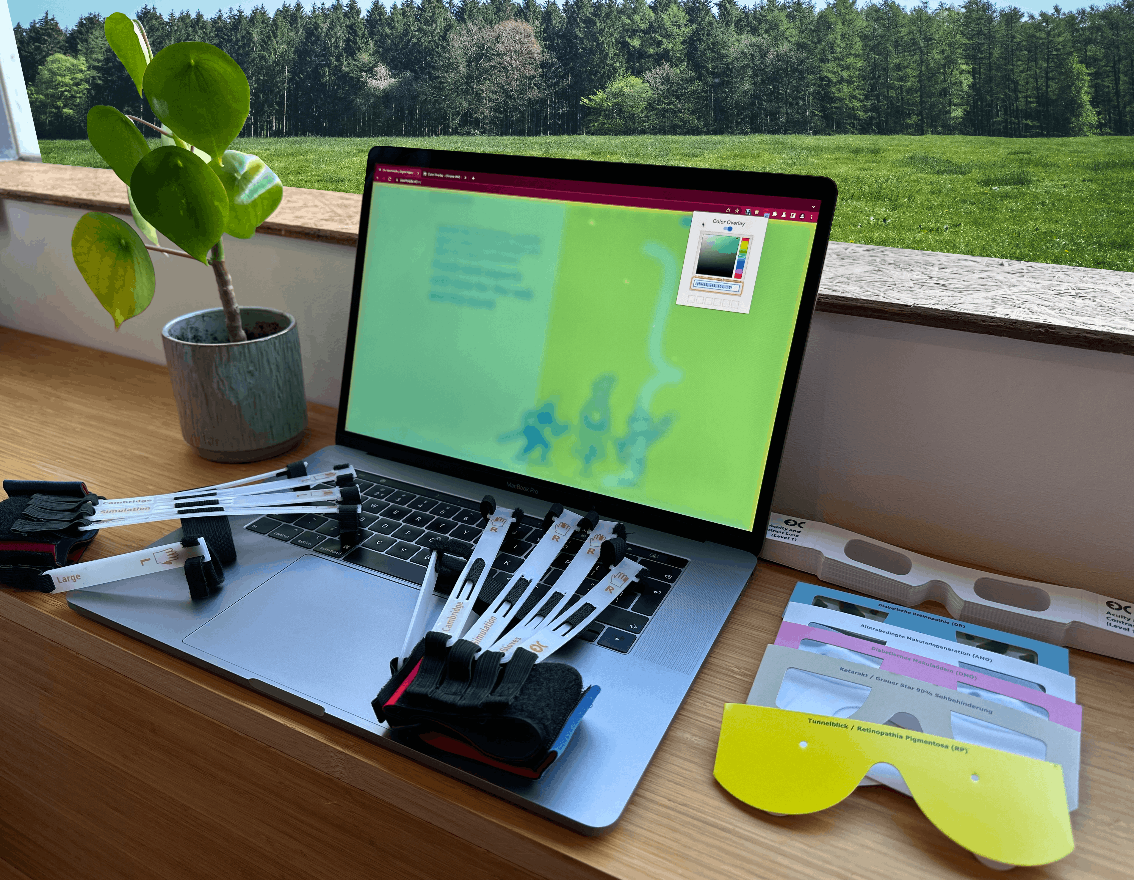 A desk with a laptop on it where a color a screenfilter is active. On top of the keyboard are simulation gloves. Next to the laptop are lying simulation glasses.