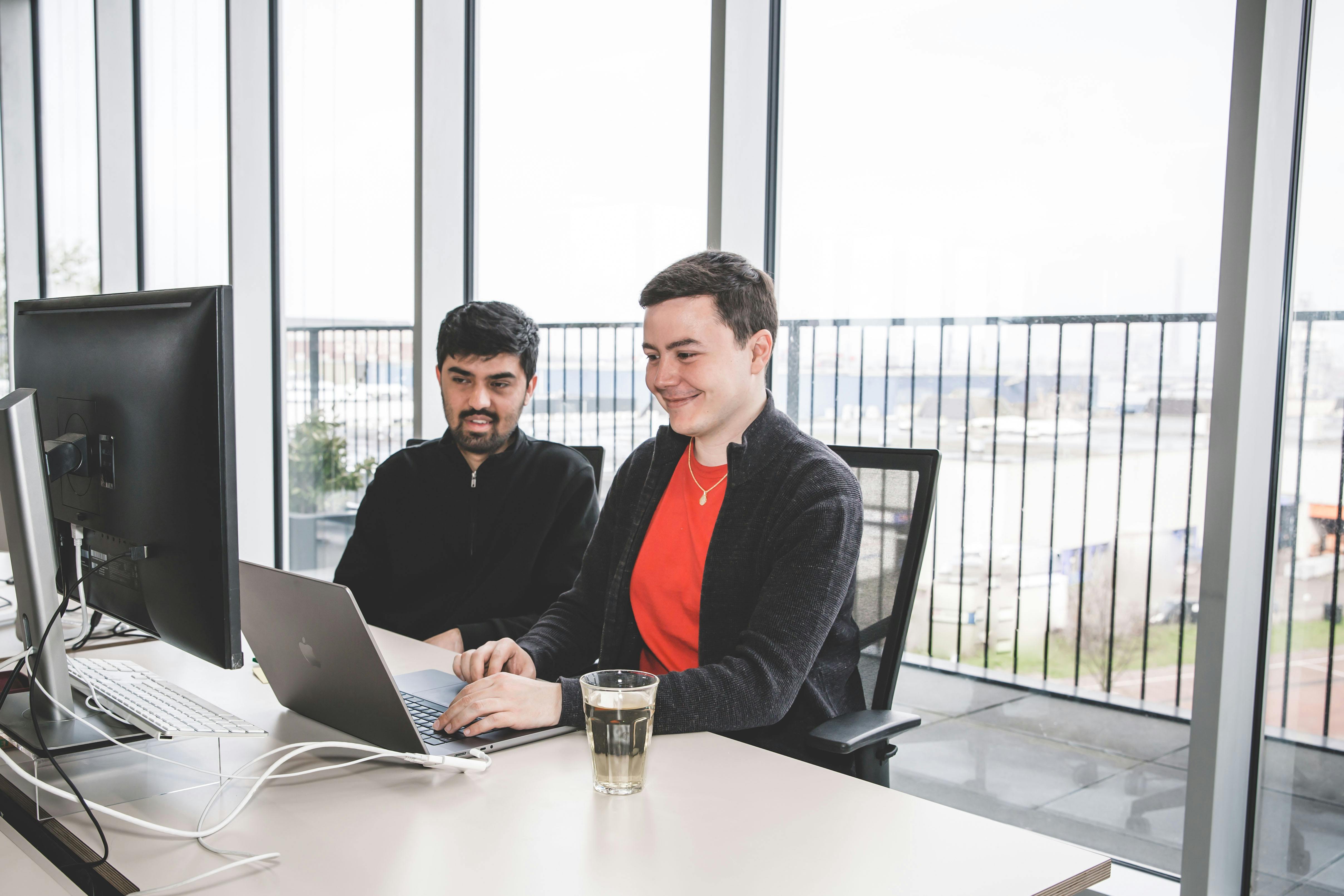 Two men looking at a desktop screen, one is typing on a laptop