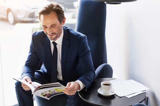 Man in pak leest magazine met kopje koffie