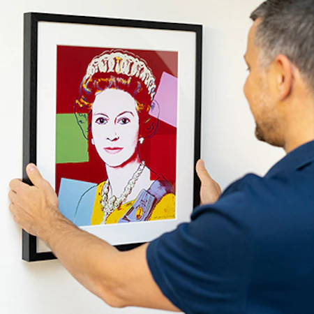Image of Showpiece collector hanging a framed replica of Andy Warhol's 'Reigning Queens' 3/3