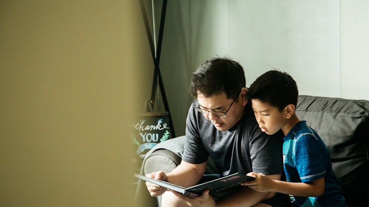 A dad and his son read a book together at home