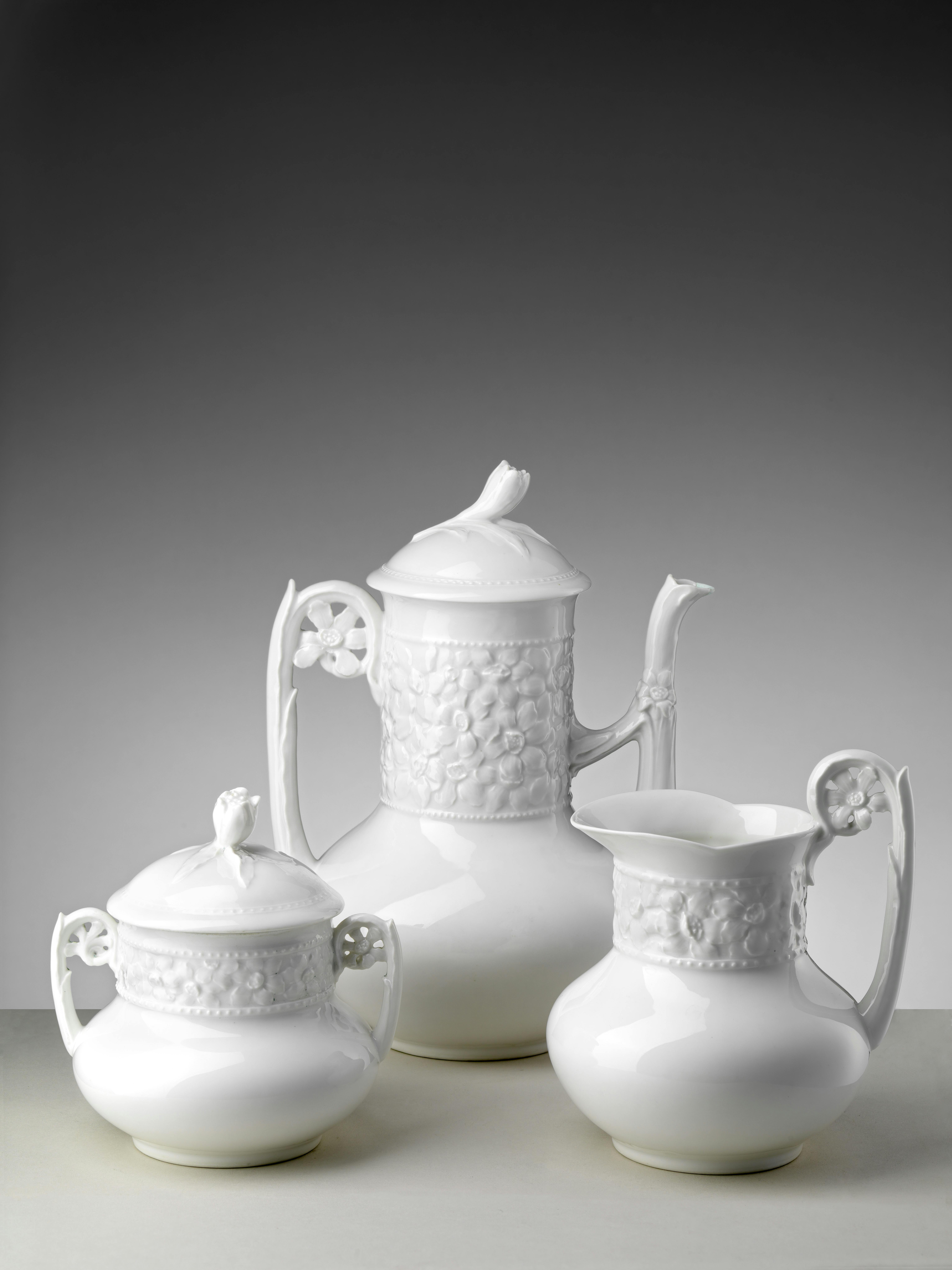 Three tableware pieces in white porcelain with stem handles and bodies decorated with raised daisies