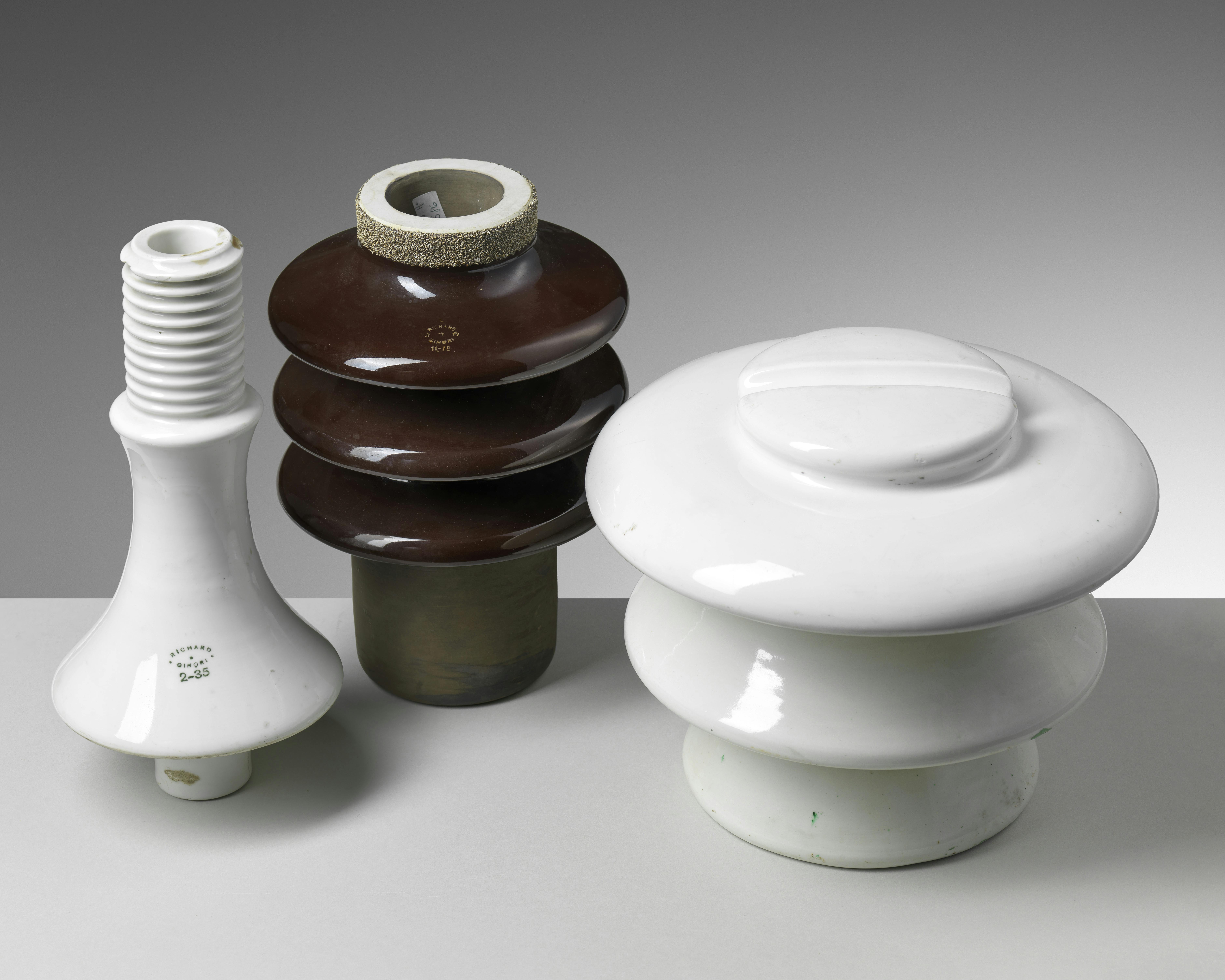 Tre isolatori in ceramica, due bianchi e uno bruno, di diverse forme e dimensioni.