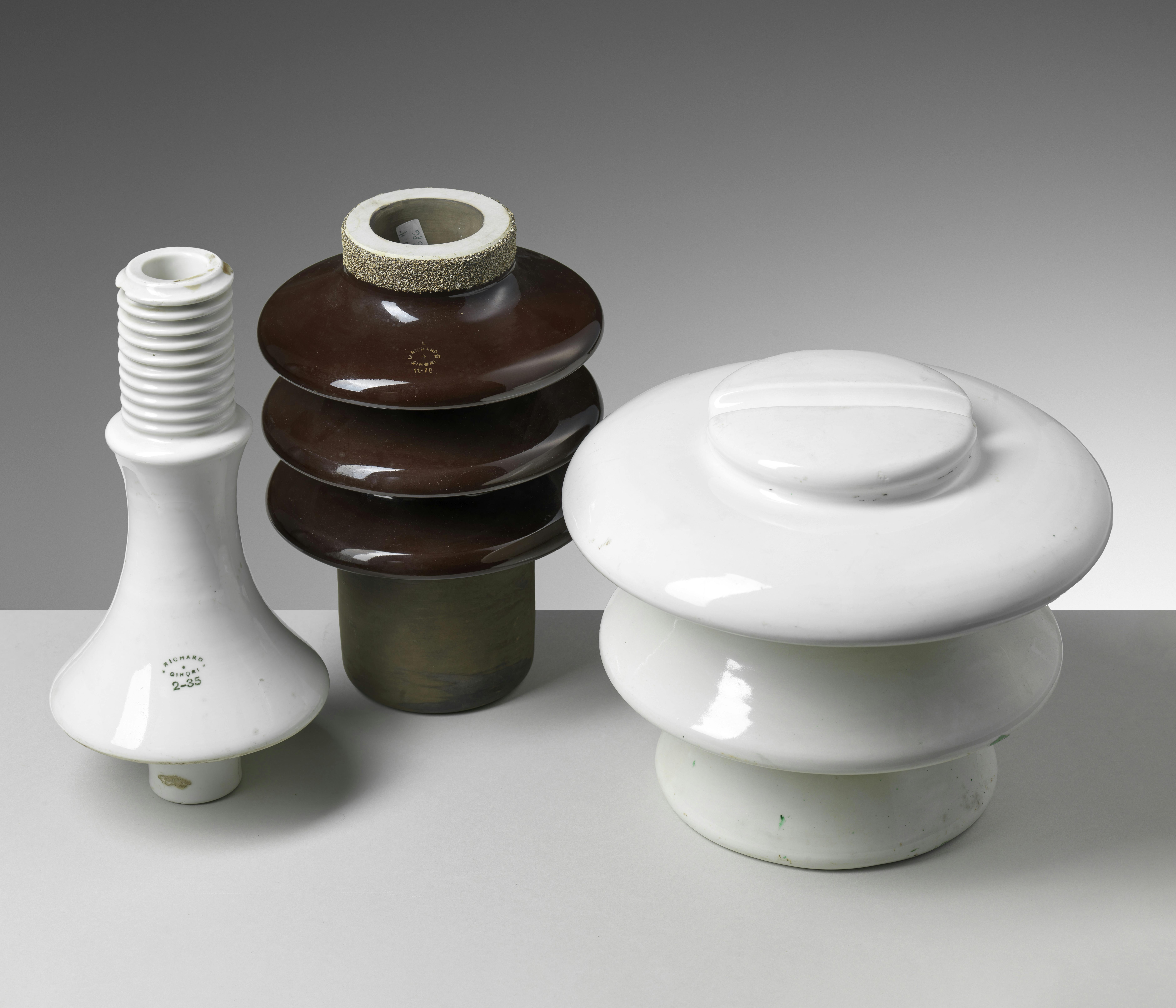Tre isolatori in ceramica, due bianchi e uno bruno, di diverse forme e dimensioni.