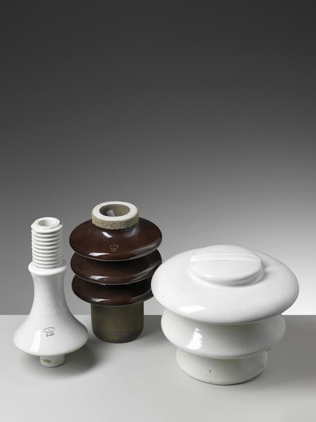 Tre isolatori in ceramica, due bianchi e uno bruno, di diverse forme e dimensioni.