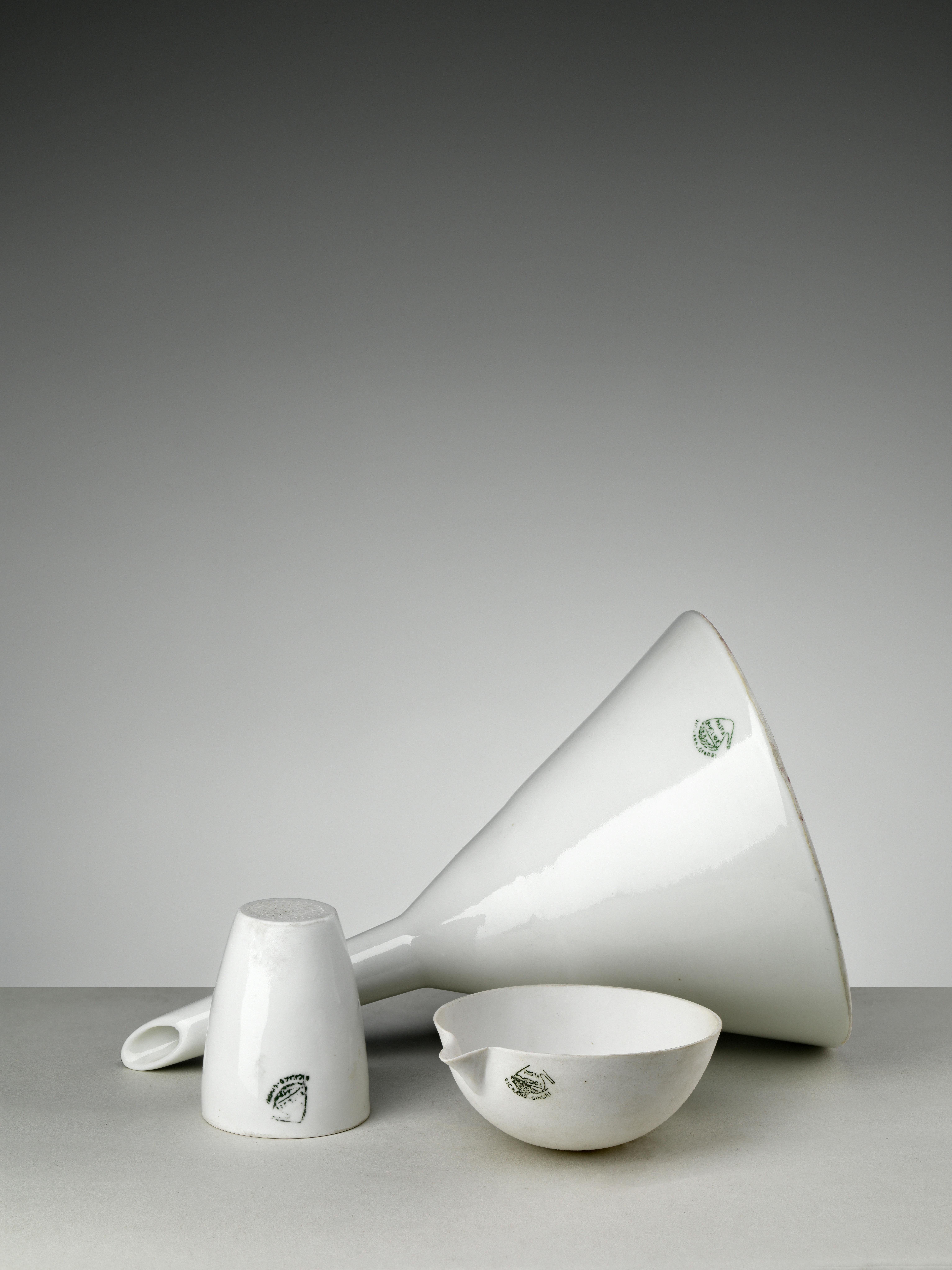Three white laboratory porcelain objects: a crucible with perforated bottom, a funnel, and a capsule with spout