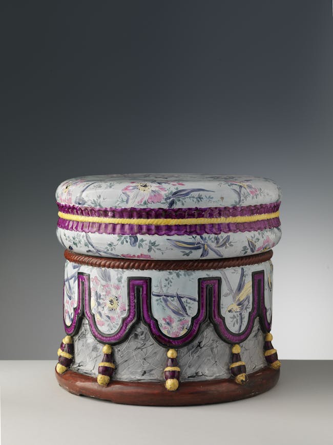 Seduta interamente realizzata in maiolica, a base circolare decorato con fiori colorati, pendoni viola e nappe