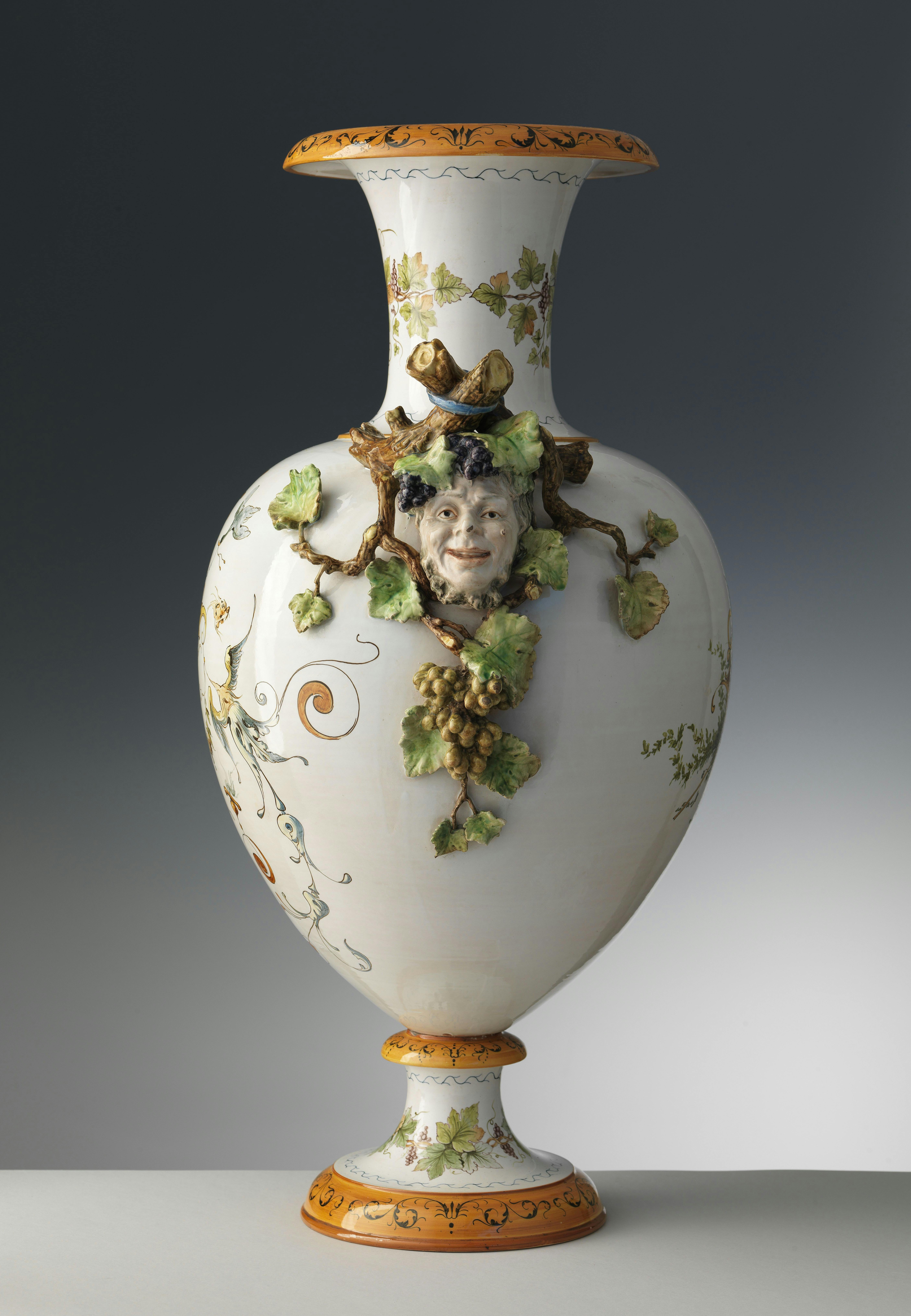 Vaso bianco con bordi arancio e decorazione policrome in rilievo con al centro una testa di Bacco