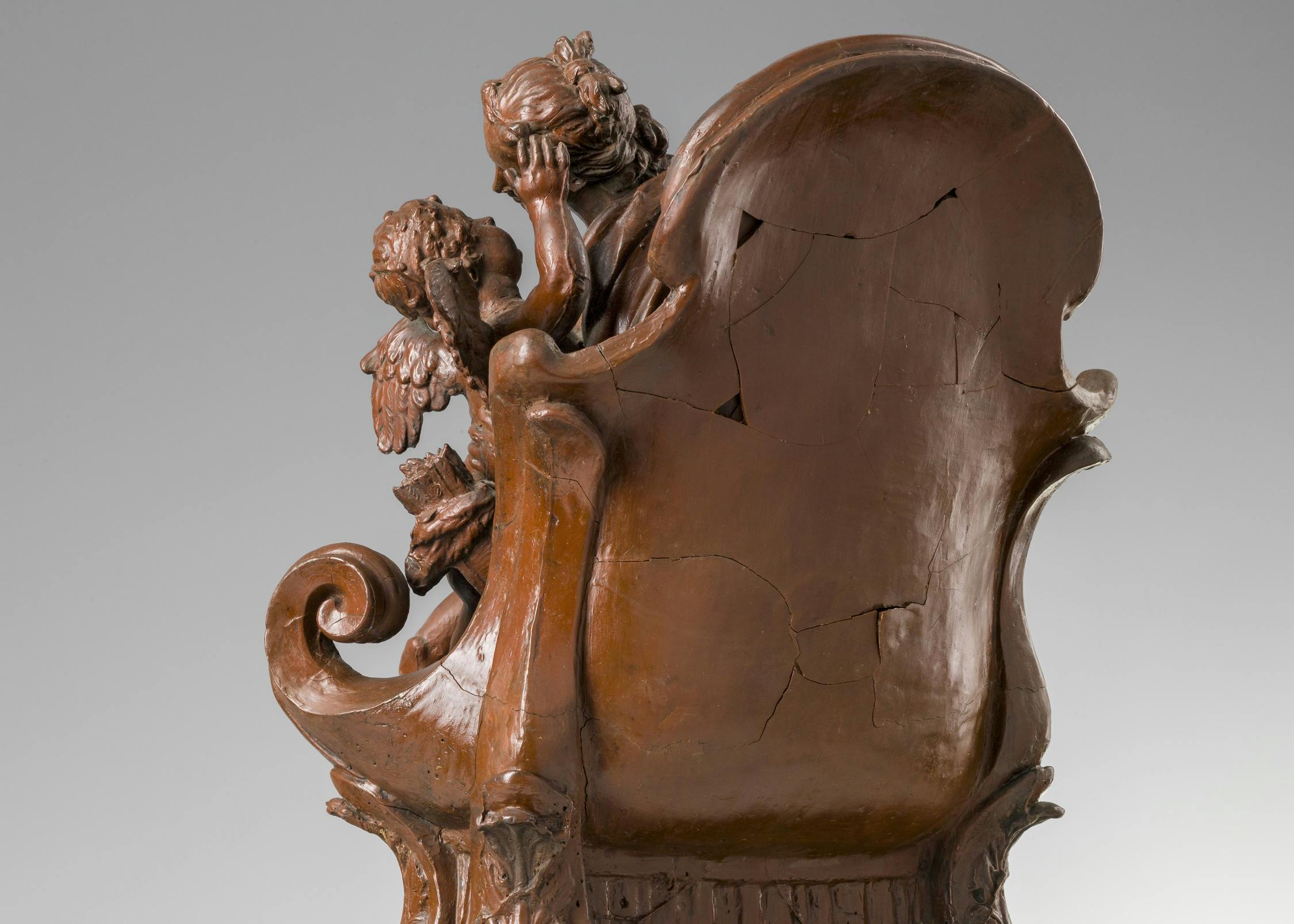 vista di tre quarti della scultura, con un seggio su cui siede una figura femminile con in braccio iun bambino