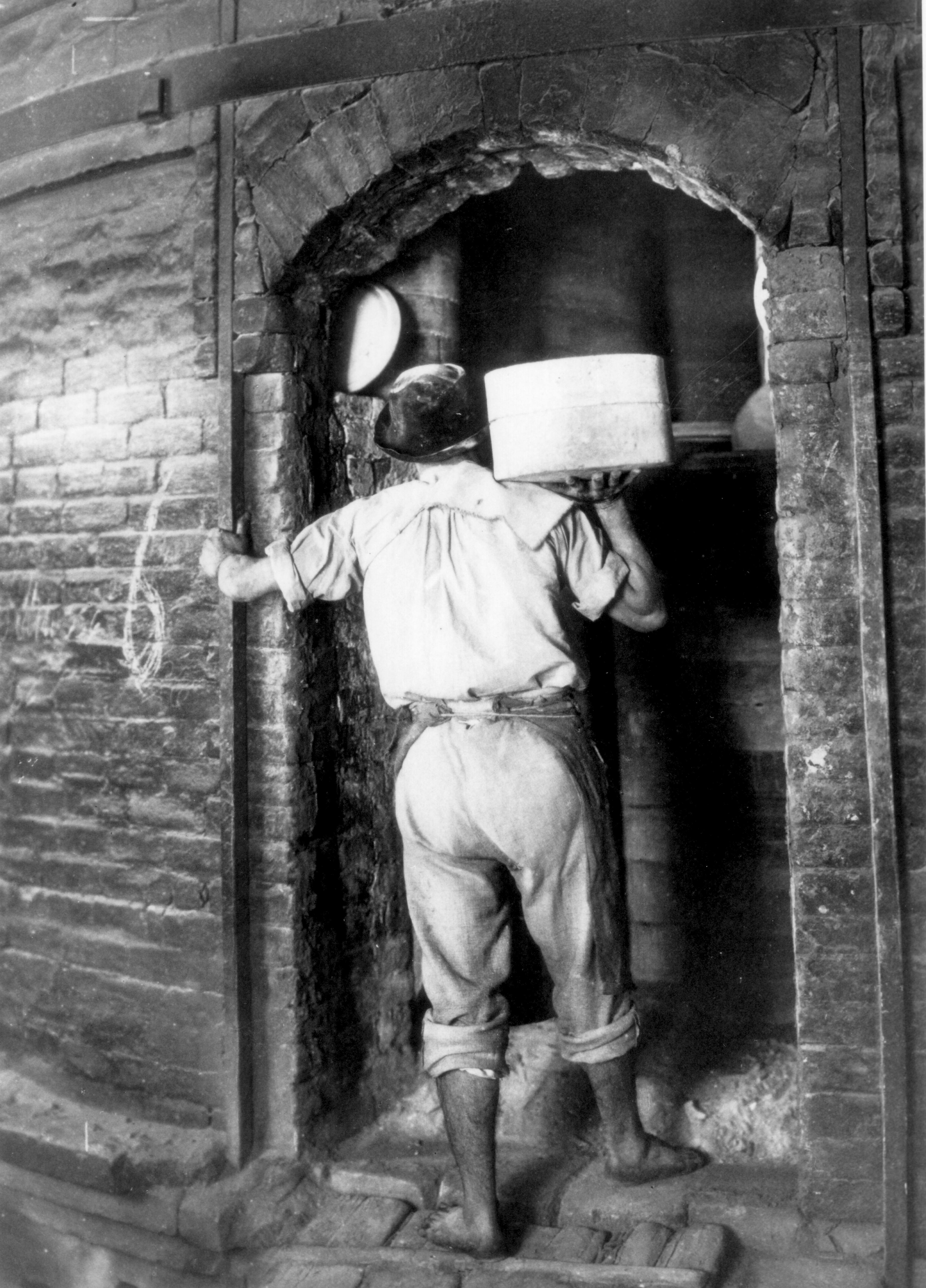 Un uomo in abiti da lavoro fotografato in bianco e nero mentre entra in un forno