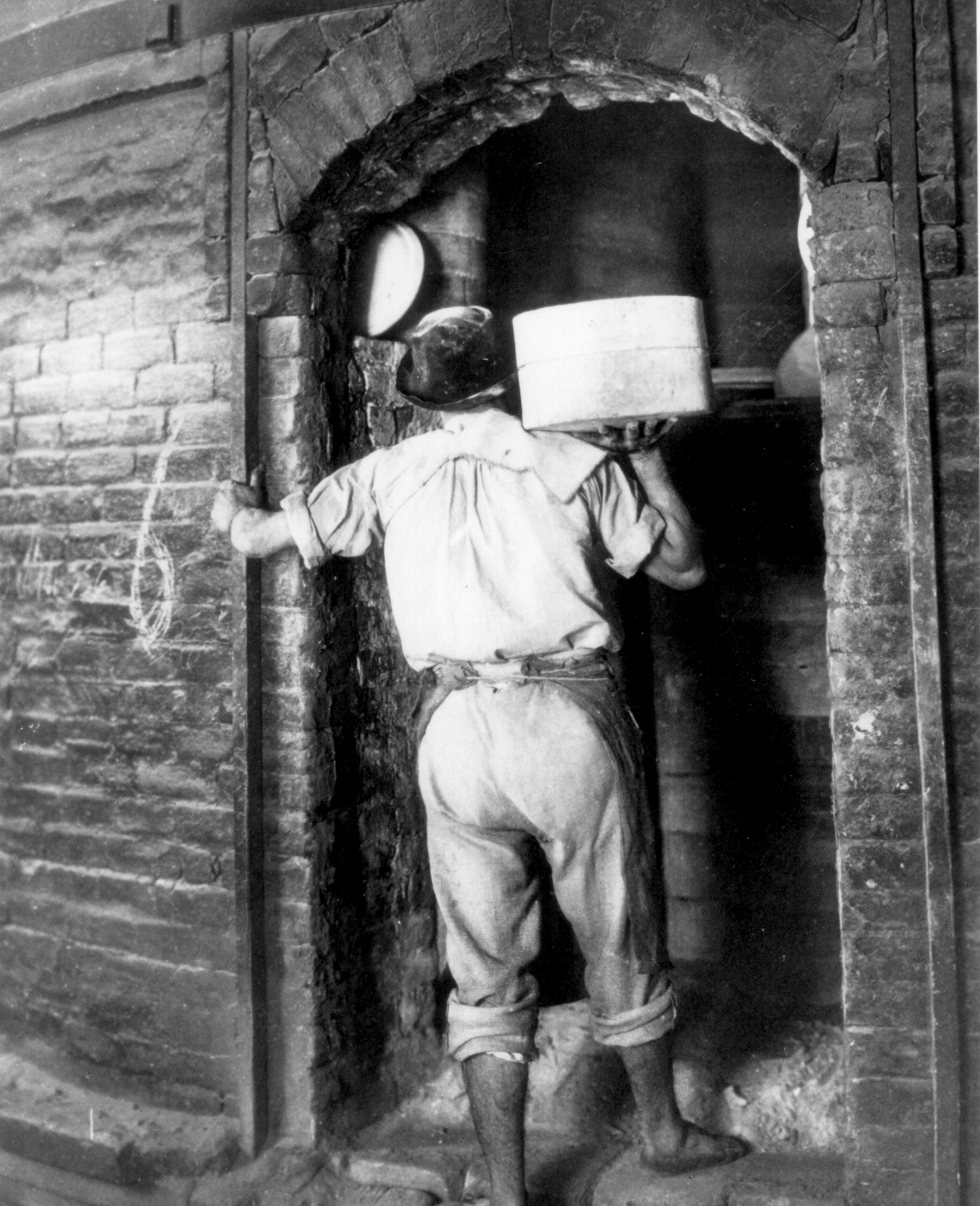 Un uomo in abiti da lavoro fotografato in bianco e nero mentre entra in un forno