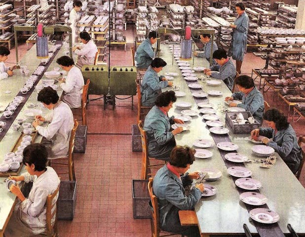 Un gruppo di operaie sedute intorno a dei tavoli e intente ad applicare decori