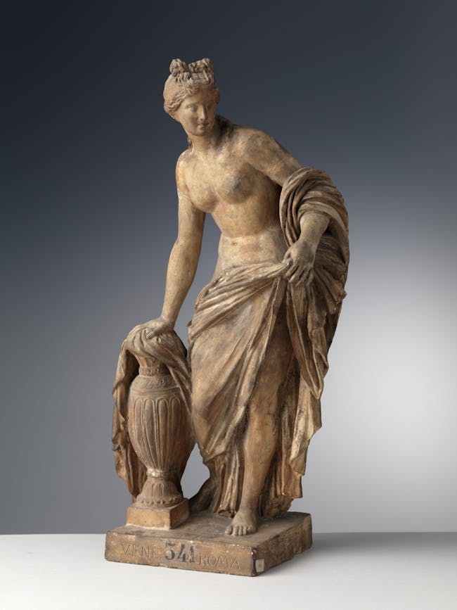 La scultura raffigua una donna coperta da un ampio panno che appoggia la mano su un'anfora