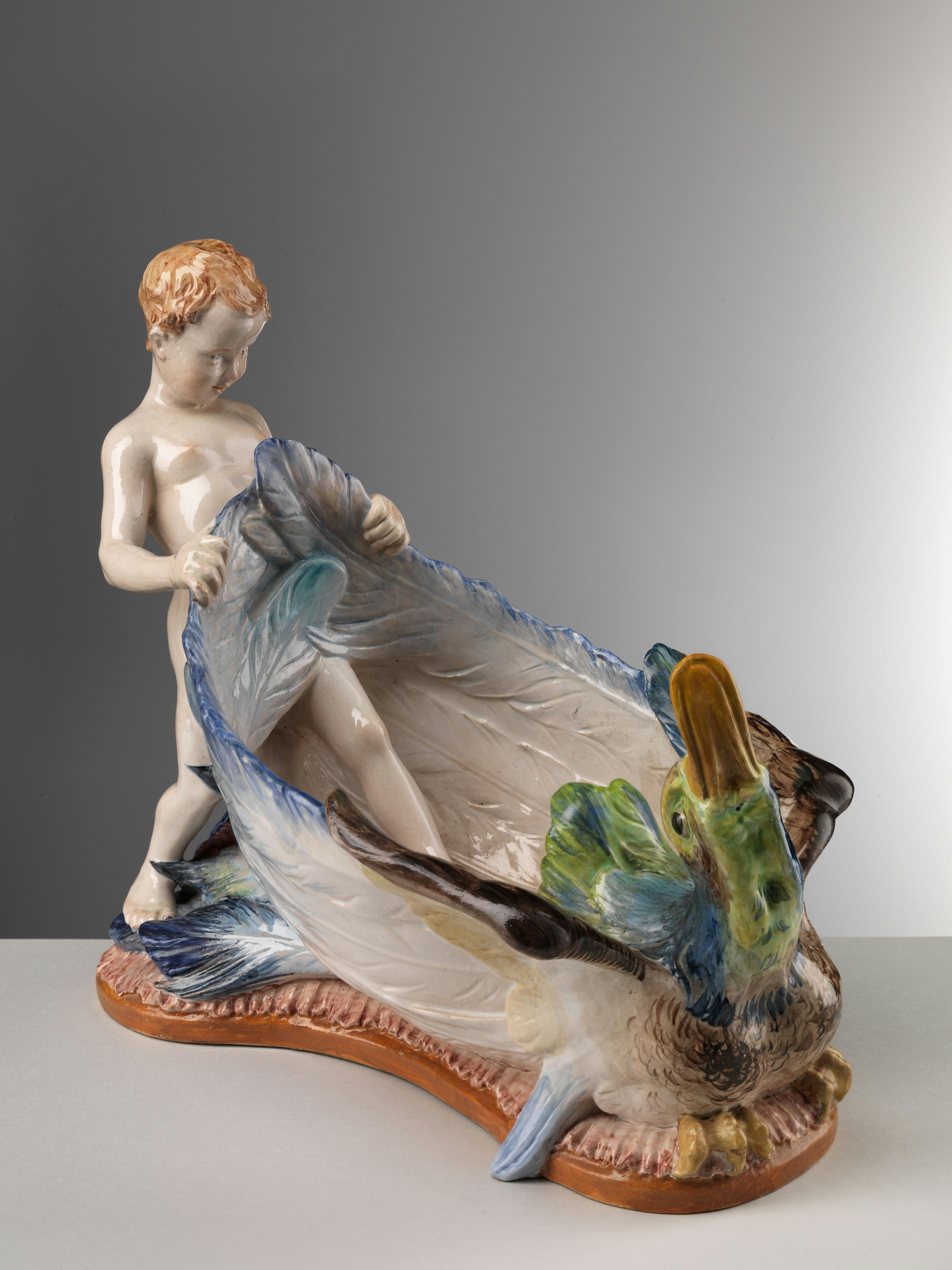 Recipiente colorato a forma di anatra sulla cui coda poggia un putto
