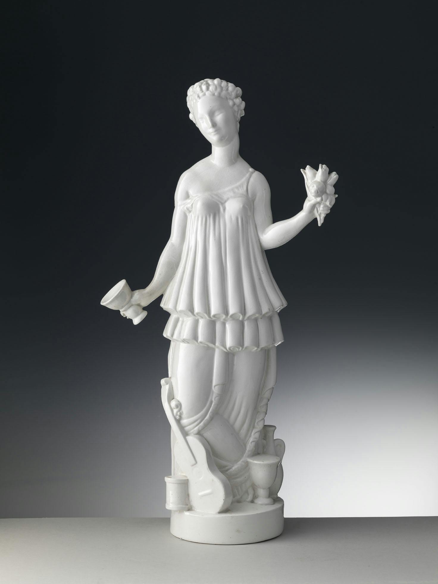 Statuetta bianca raffigurante una figura umana con vari oggetti in mano e ai piedi