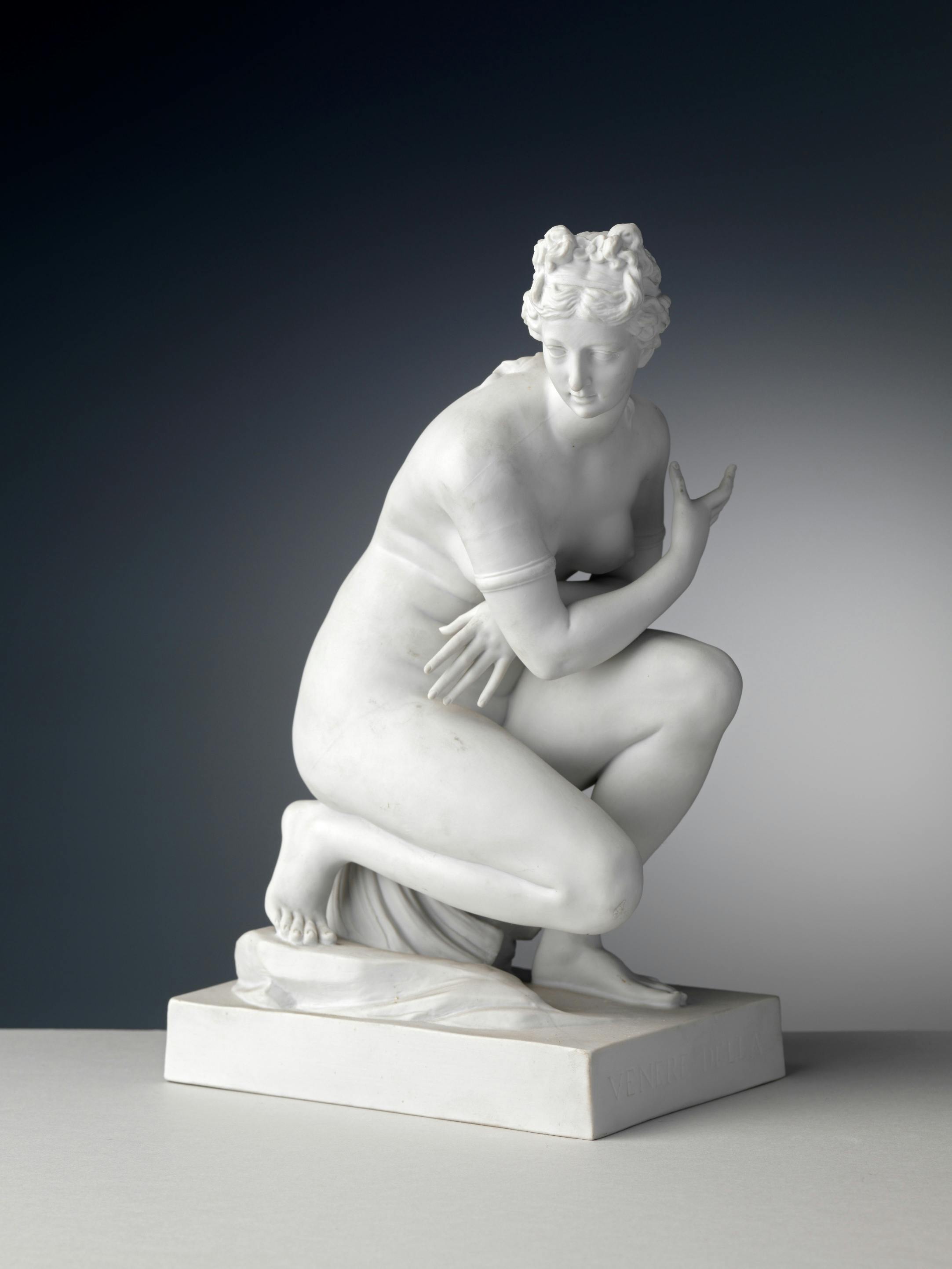 Scultura bianca di figura femminile nuda inginocchiata su una conchiglia