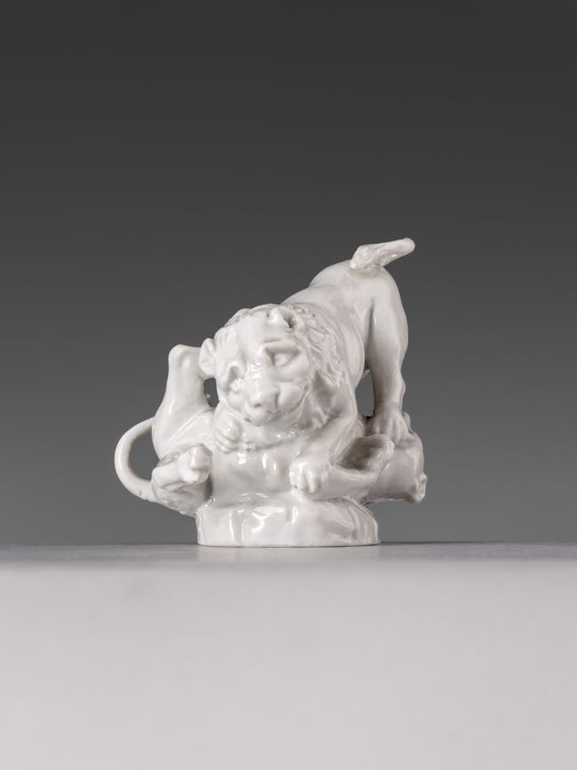 Piccola scultura in porcellana bianca raffigurante un cane assolito da un leone