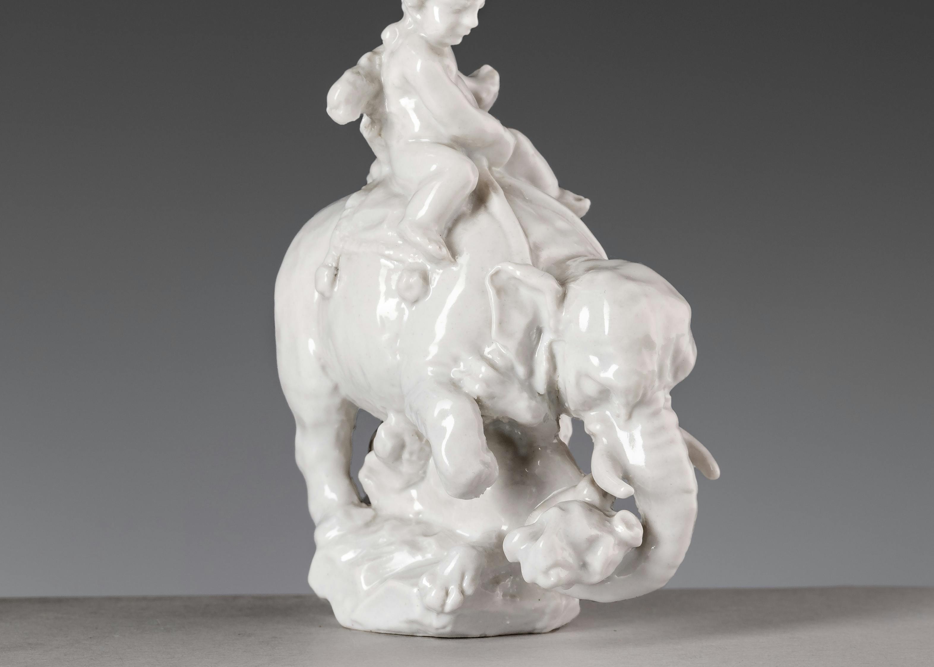 Piccola scultura di porcellana bianca raffigurante un bambino a cavallo di un elefante