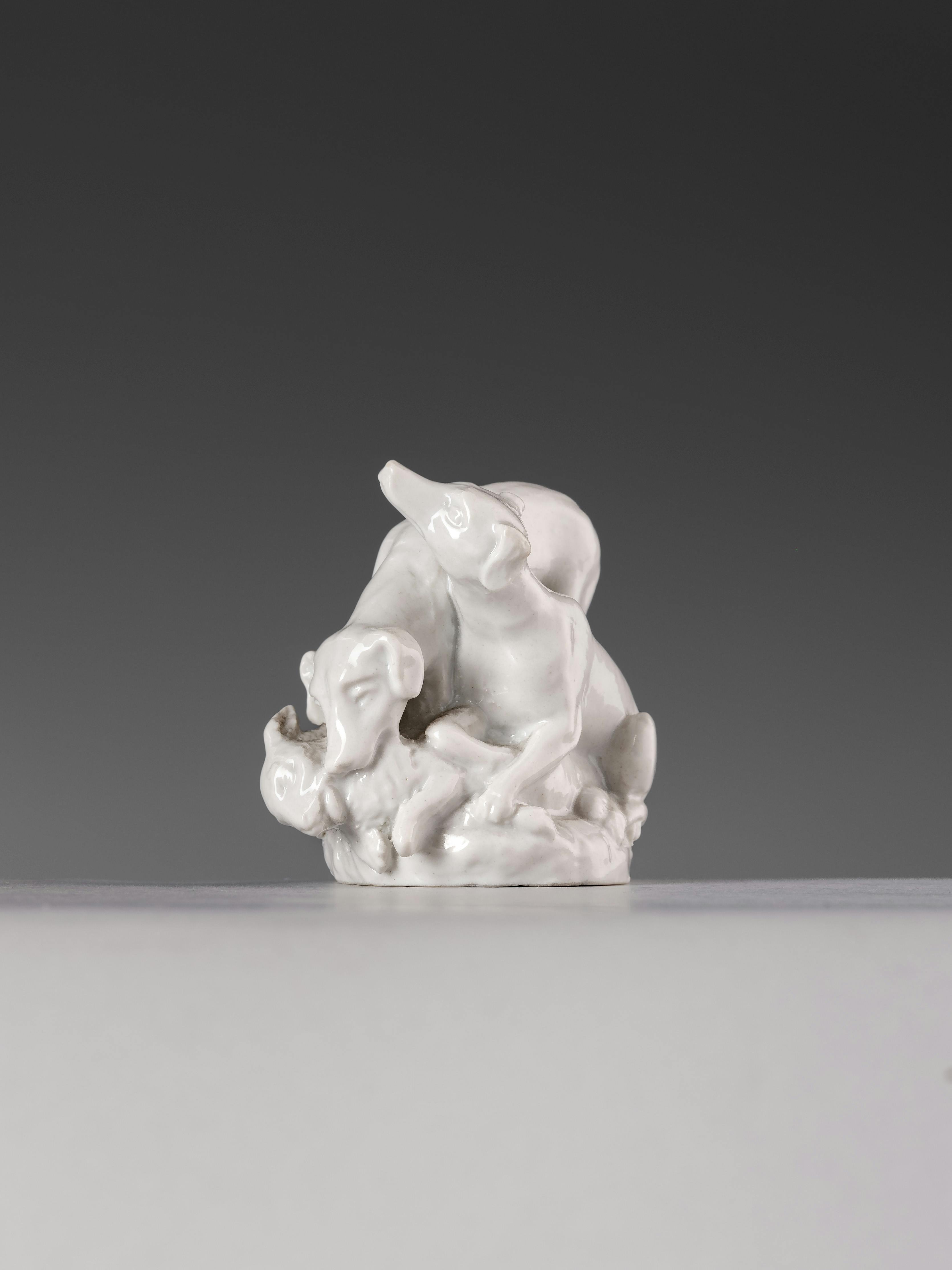 Piccola scultura in porcellana bianca che raffigura due cani che catturano un coniglio