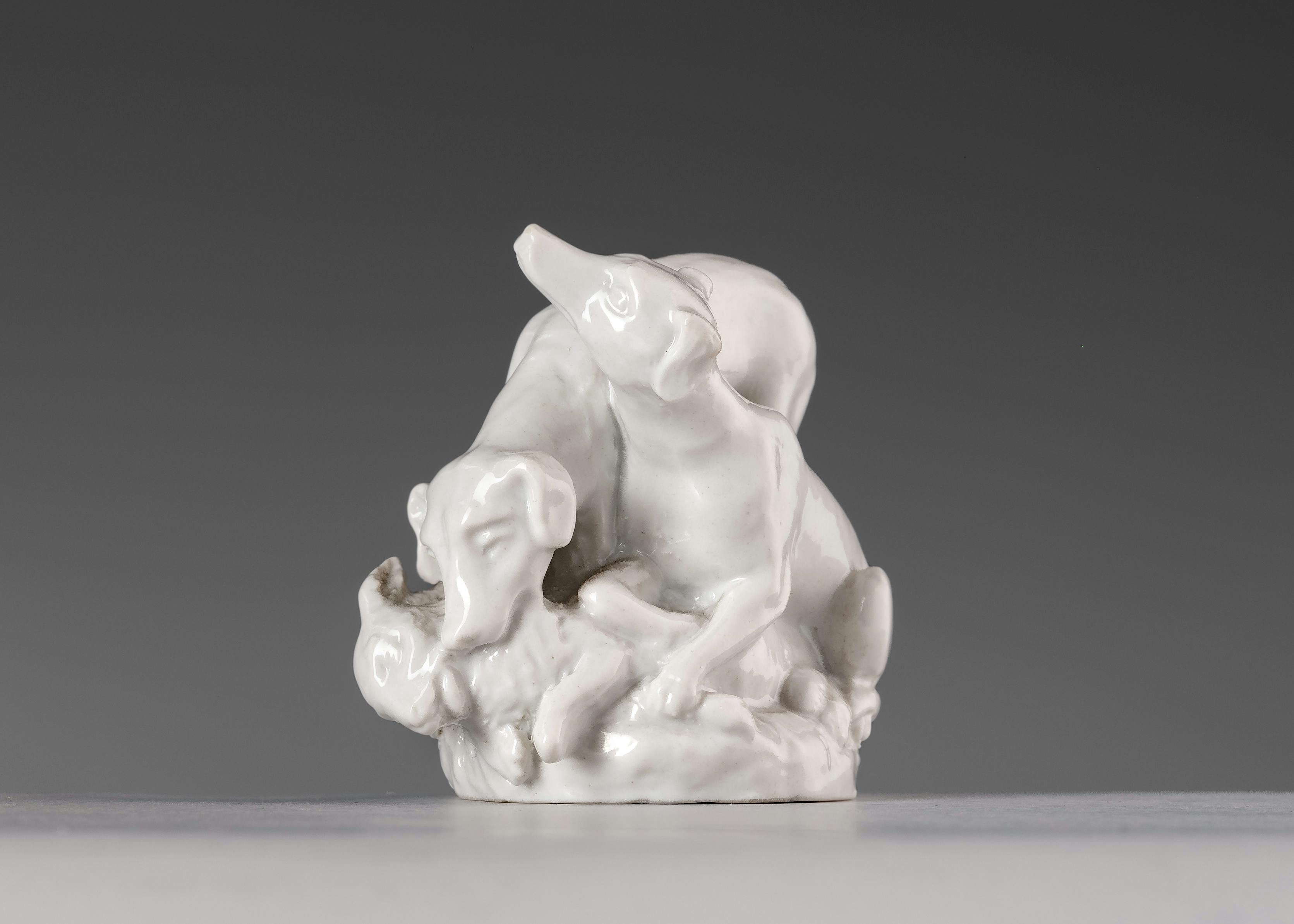 Piccola scultura in porcellana bianca che raffigura due cani che catturano un coniglio