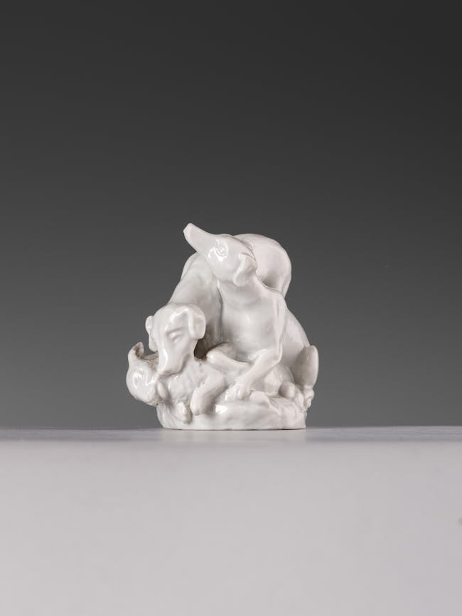 Piccola scultura in porcellana bianca che raffigura due cani che catturano un coniglio