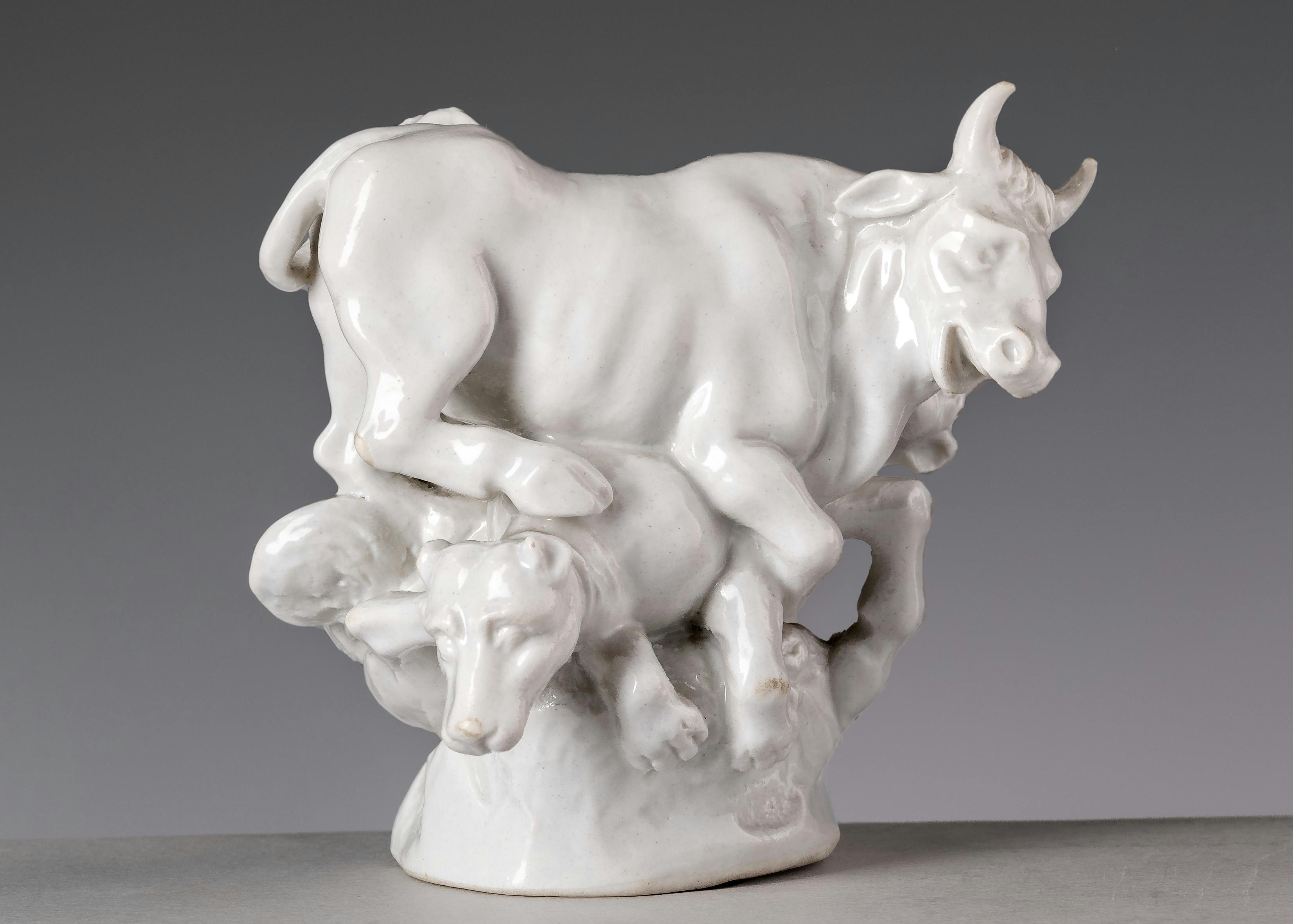 Piccola scultura in porcellana bianca raffigurante un toro e due cani che compattono