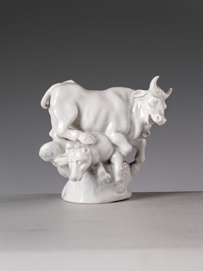 Piccola scultura in porcellana bianca raffigurante un toro e due cani che compattono