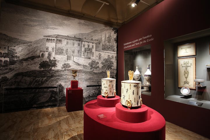 In primo piano due ciste in porcellana bianca e oro. sullo sfondo altre opere e una veduta della Manifattura Ginori