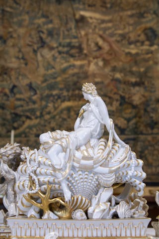 Scultura bianca con decori oro, raffigurante una figura femminile appoggiata su una conchiglia