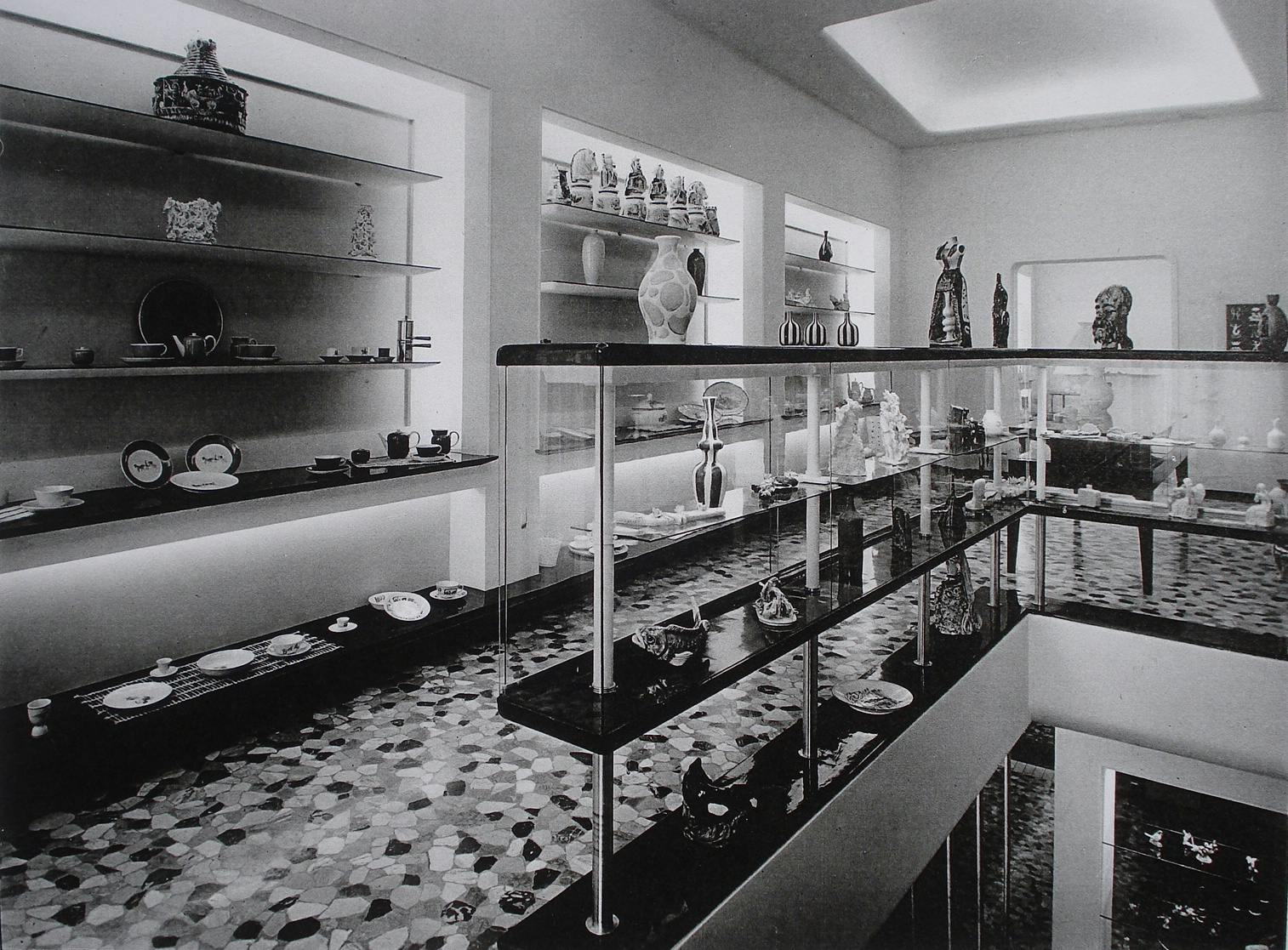 Foto in bianco e nero di un negozio con espositori su cui poggiano oggetti ceramici e sculture