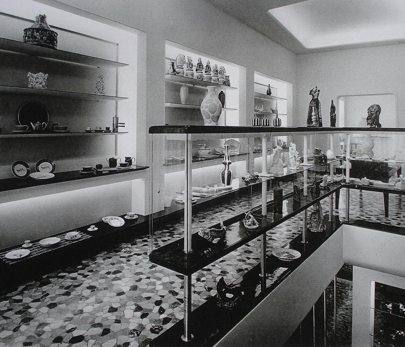 Foto in bianco e nero di un negozio con espositori su cui poggiano oggetti ceramici e sculture