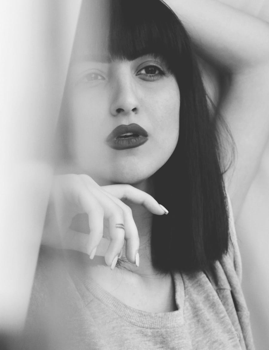 Woman, partially blurred, with one hand behind her head and the other next to her chin.