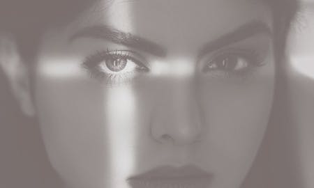 A beautiful woman's shadowed face with light making a cross on her left eye