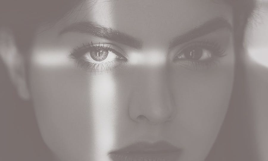 A beautiful woman's shadowed face with light making a cross on her left eye