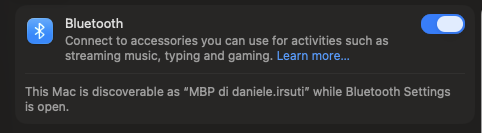 Switch Bluetooth macOS con toggle ON (blu acceso), etichette contestuali “Connect to music, typing and gaming” e stato dispositivo visibile “MBP Daniele.rsuti discoverable”.