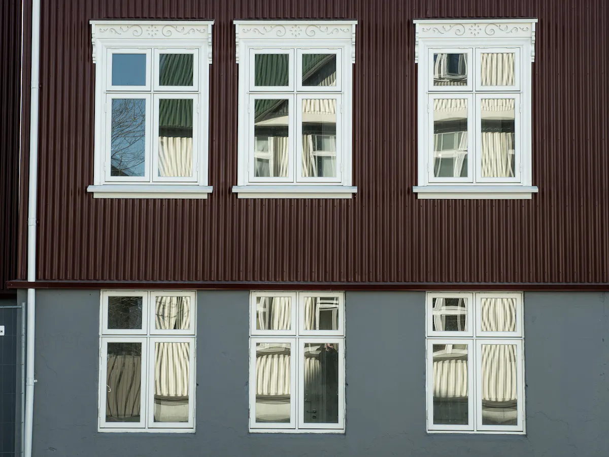 Aldamótagluggar með flúruðum körmum að ofan Hvítir aldamótagluggar á bárujárnshúsi með flúri á körmum