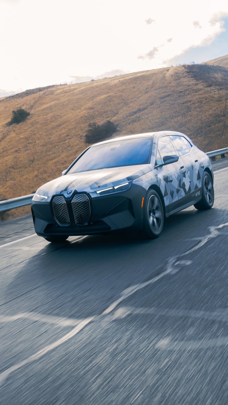 Camouflaged test vehicle travelling on road surrounded by rolling hills