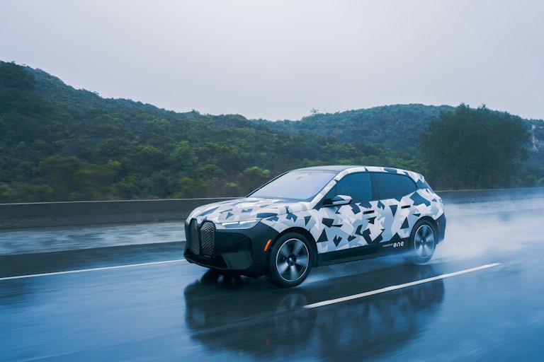 Camouflaged test vehicle powered by ONE battery driving on wet road