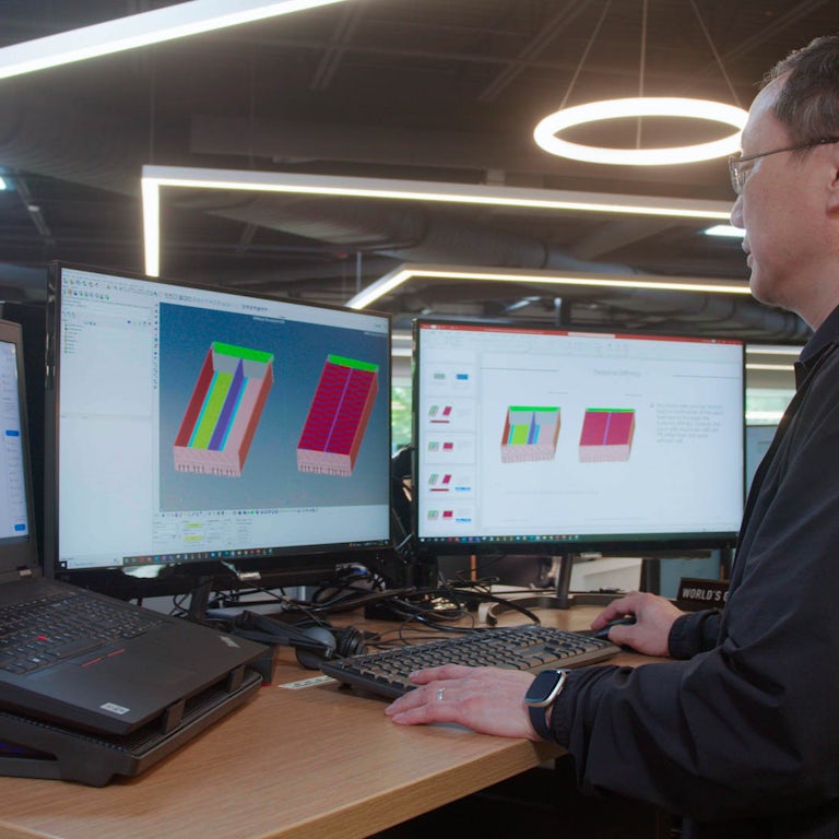 Engineer designing a battery pack with laptop and two displays