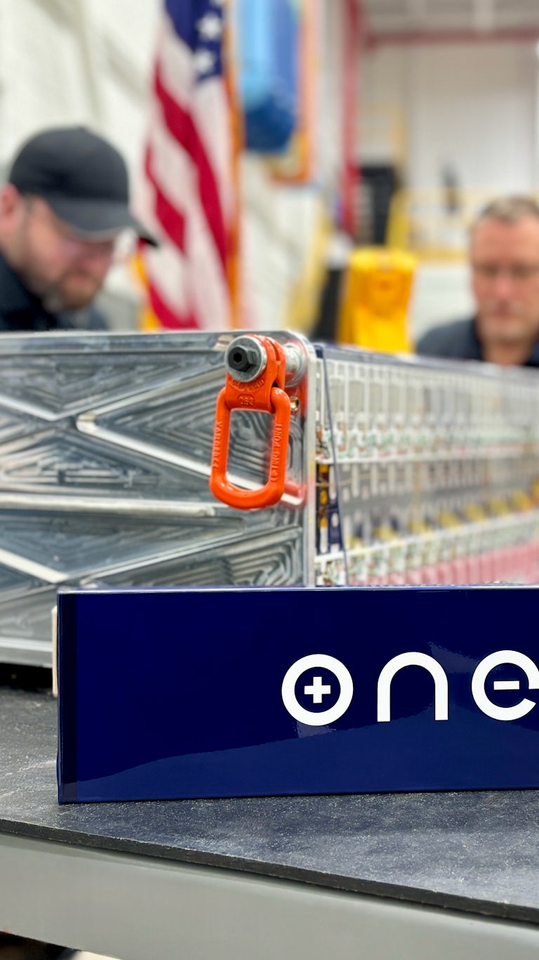 ONE OTP cell and Core 40 battery module in foreground of ONE HQ workshop with employees and American flag in background
