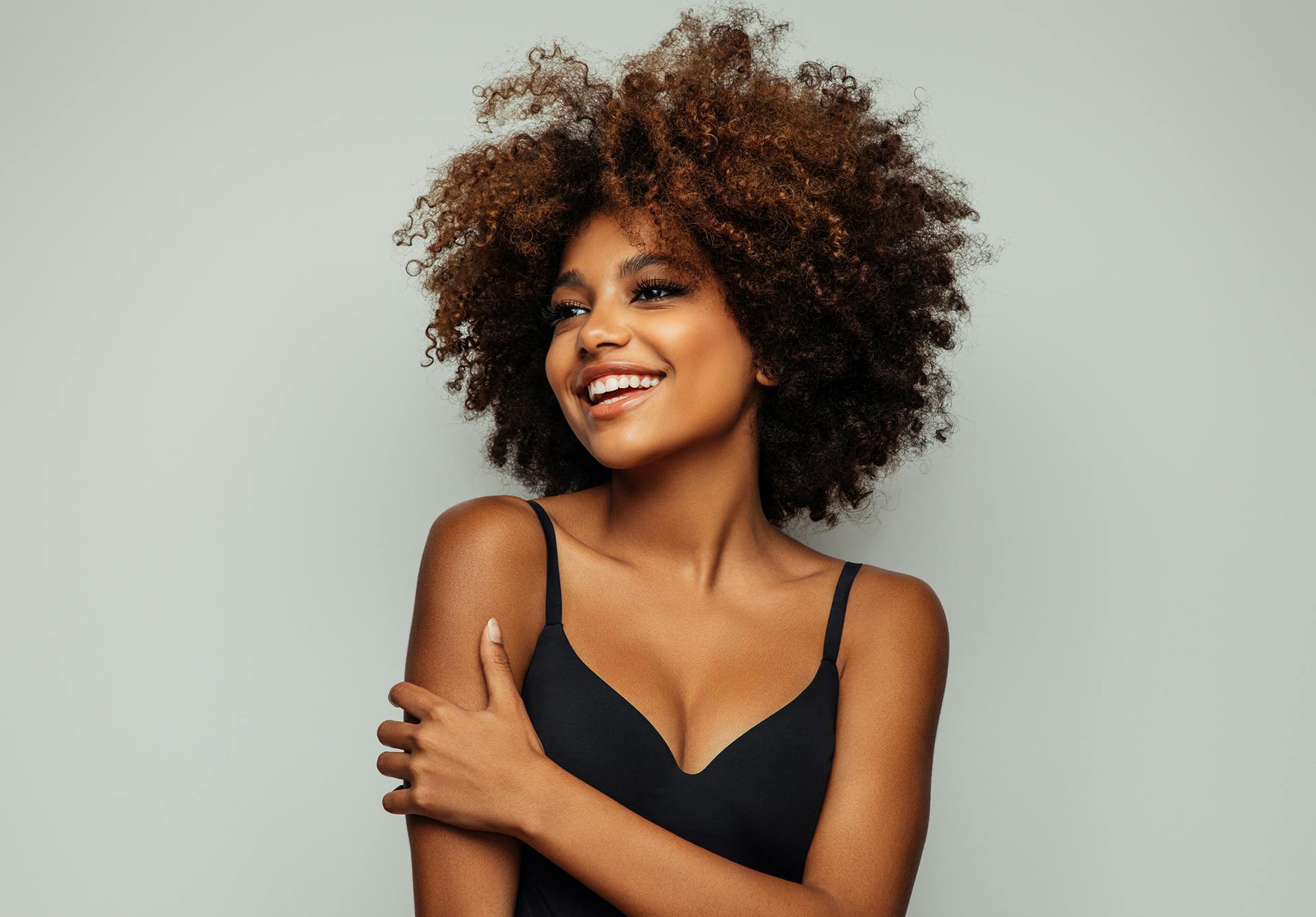 Frizzy haired woman in a black top smiling & looking to the side.