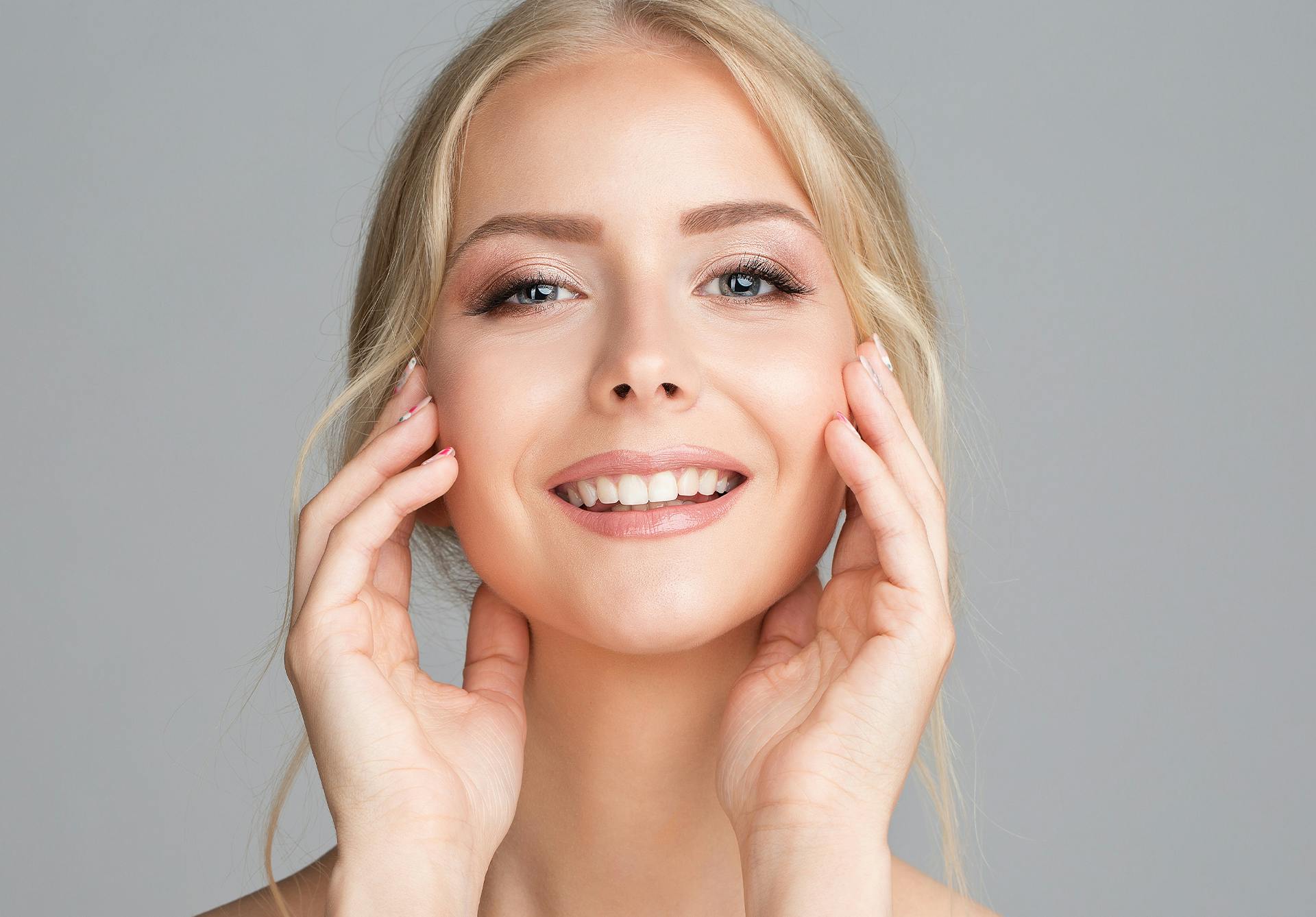 Smiling blonde woman smiling and touching her face.