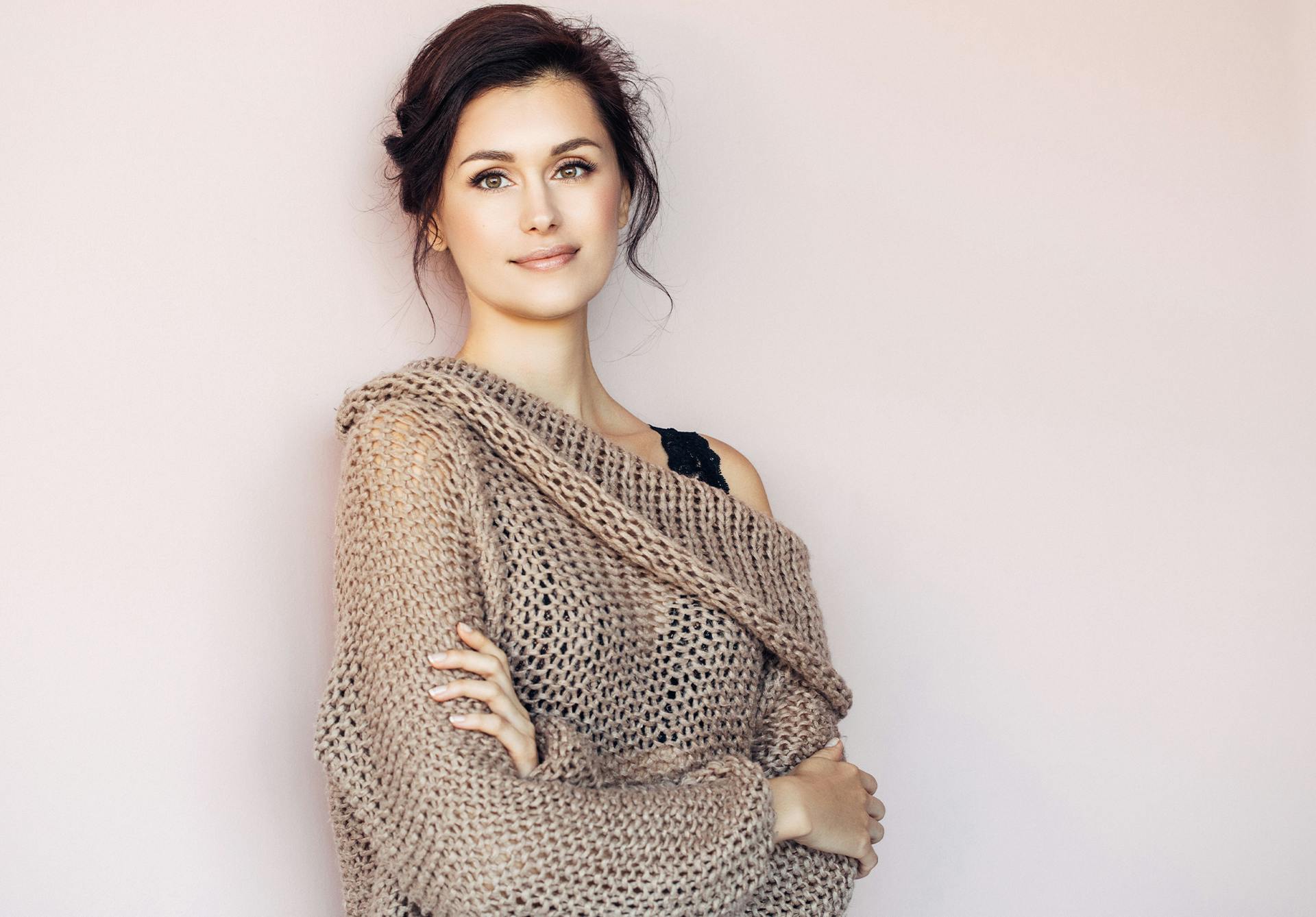 brunette woman leaning against a wall in a light brown knitted sweater