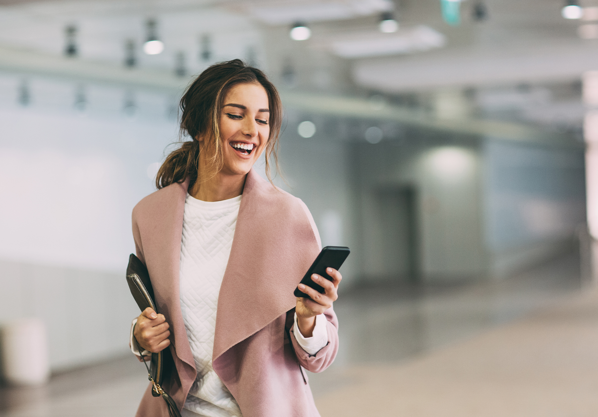 brunette in a pink coat smiling and looking at her phone