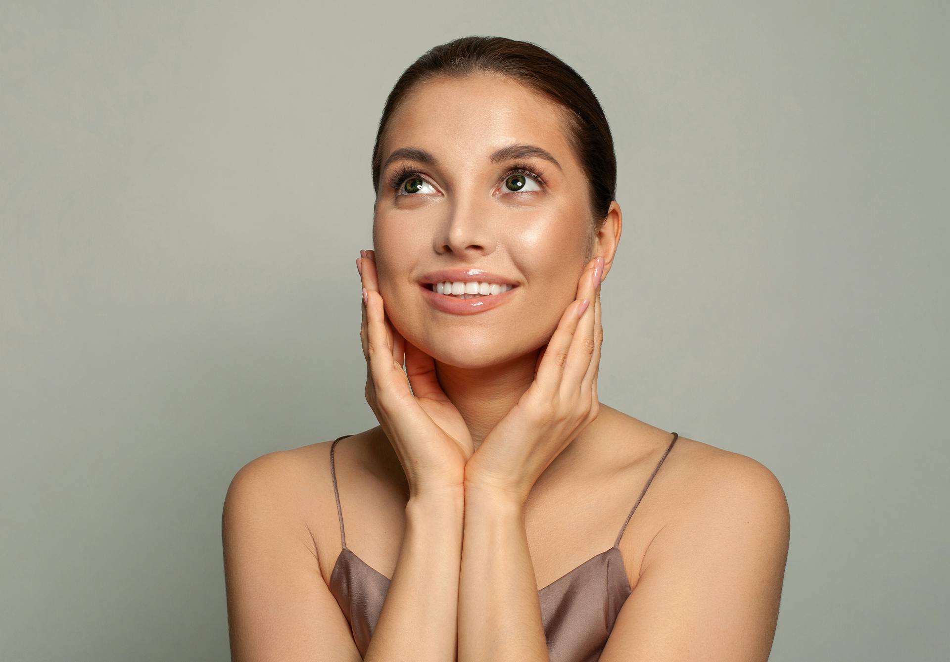 a brunette model looking upward with her hands placed on either side of her face.