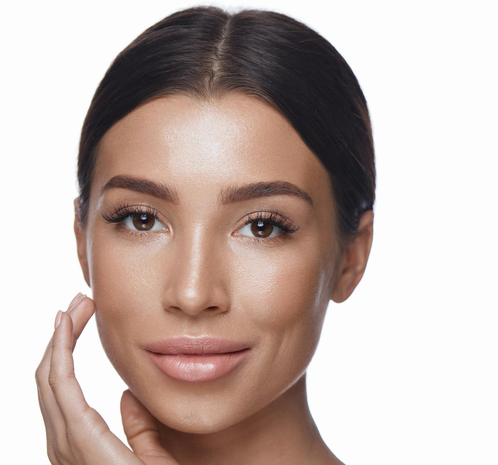 A smiling brunette woman touching her face.