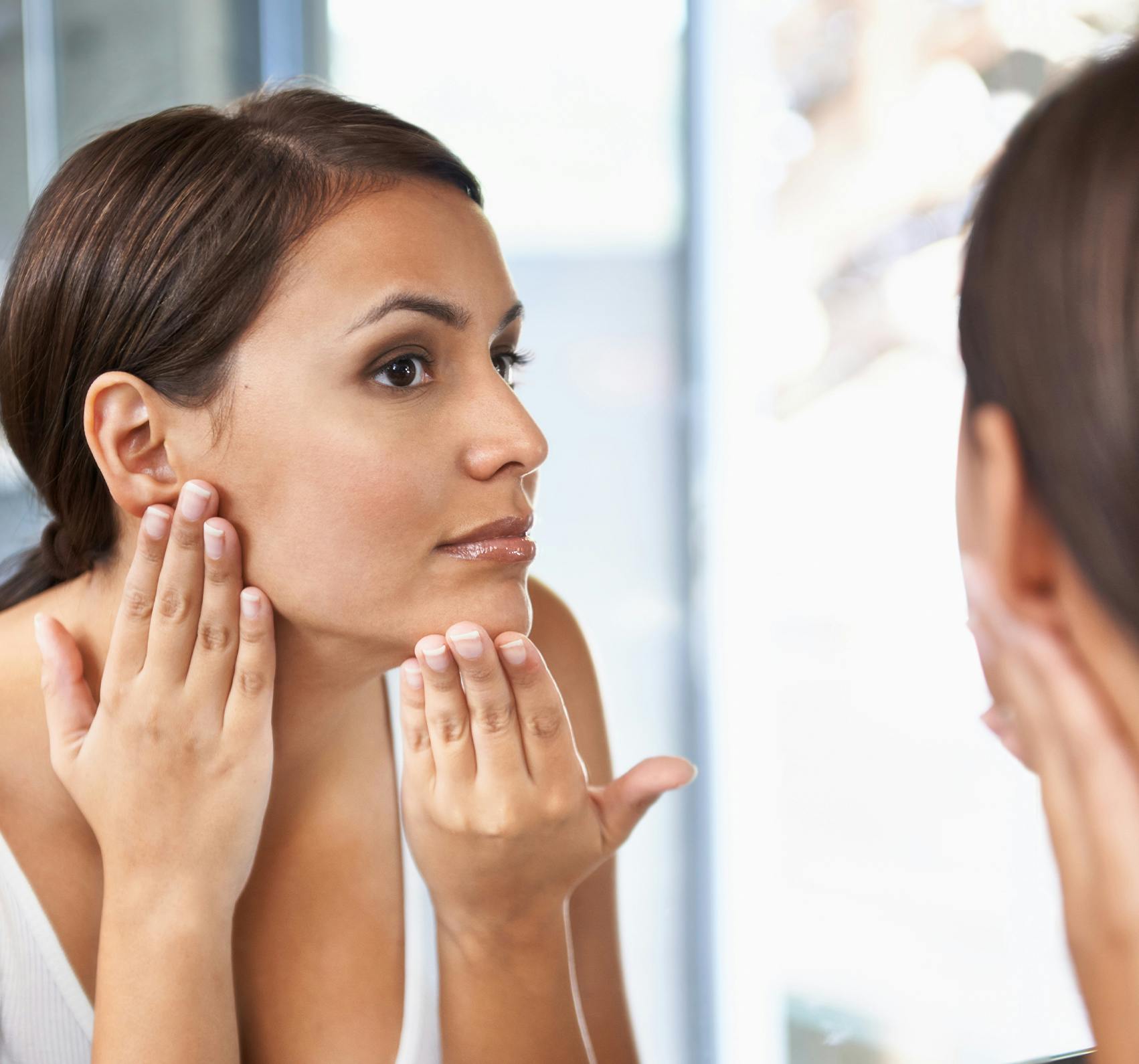 Woman looking at her face in the mirror and applying lotion.