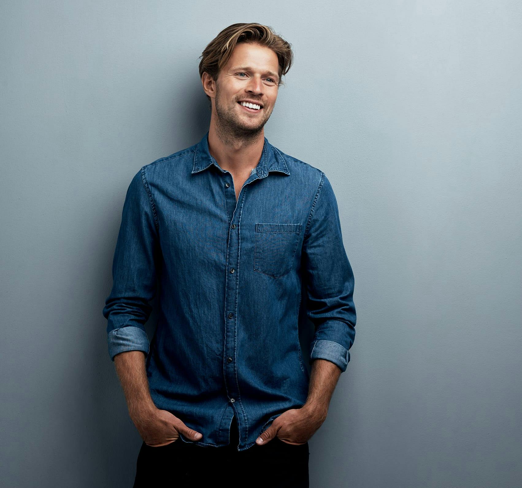 Man standing in front of a gray background wearing a blue jean jacket.