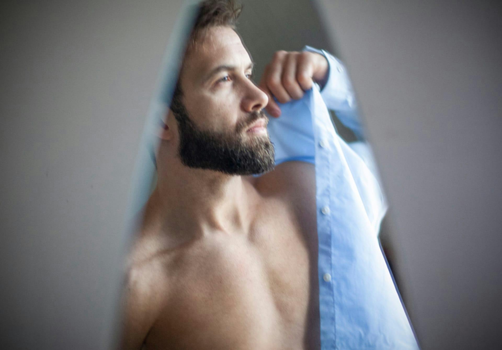 Bearded man putting on a blue shirt.